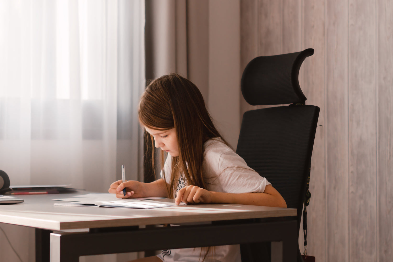 Preteen student studying at a home desk with an ergonomic high-back chair by a window with natural light